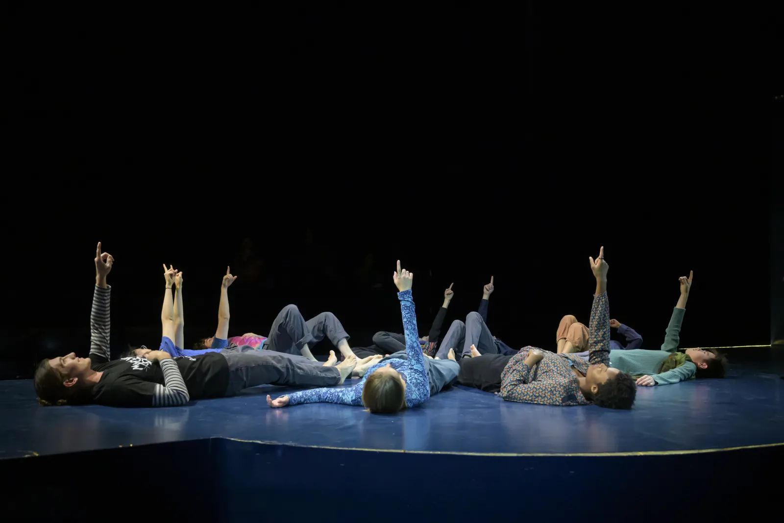 The cast of 32 Very Short Plays About Letting Go. Ten performers lay on the ground and point up to the sky. 