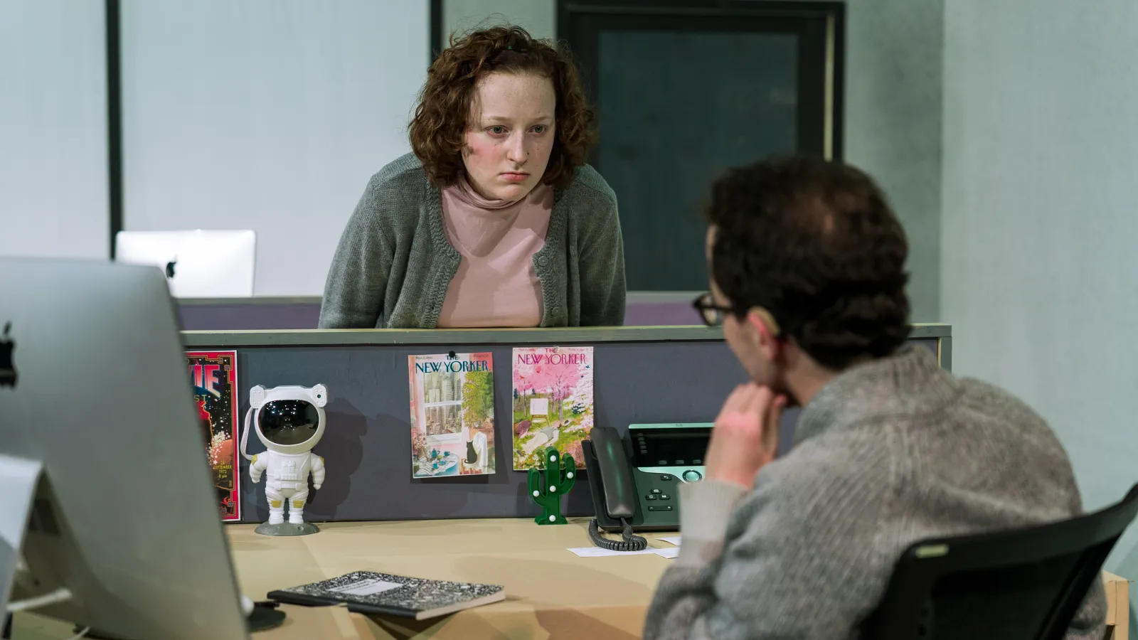 Gloria, a woman in a grey cardigan, glares at Sasha, a person sitting behind a desk 