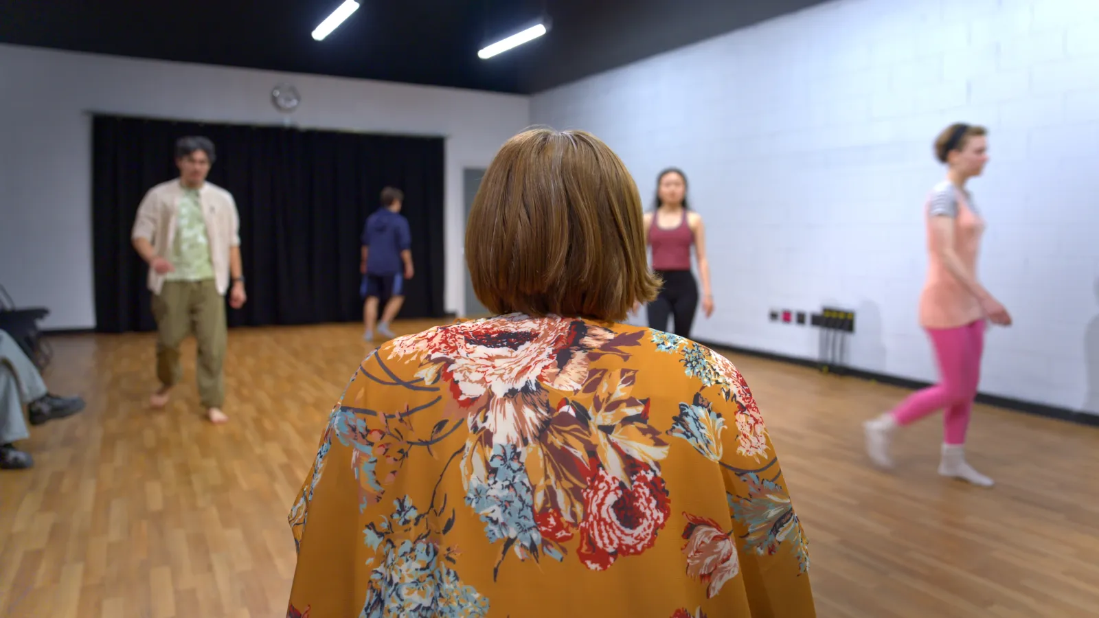 Students walk about a studio while their teacher watches on from the foreground. Faces are not distinguishable 