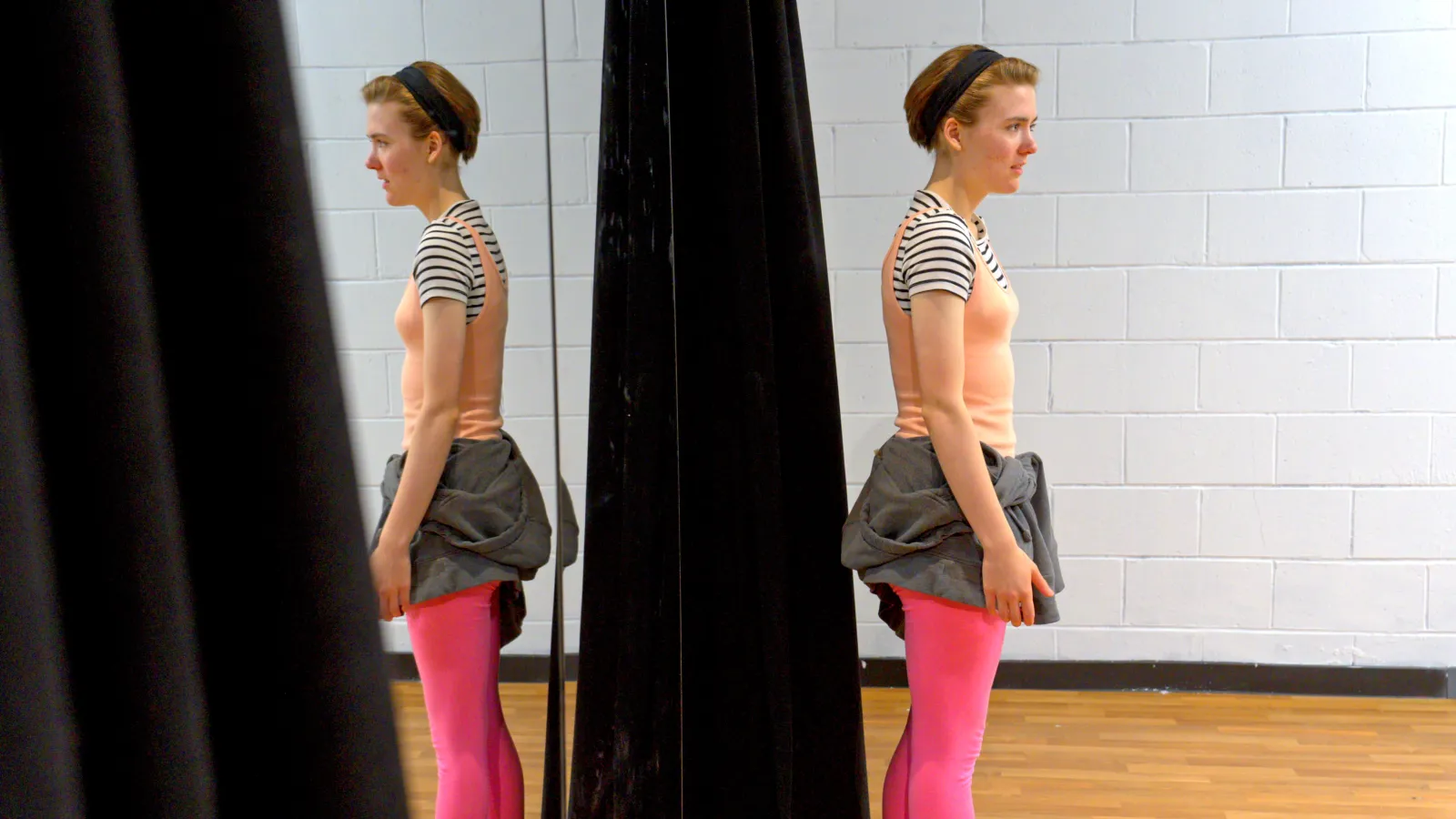 Lauren stands with her back to the mirror and her reflection gazes out in the opposite direction