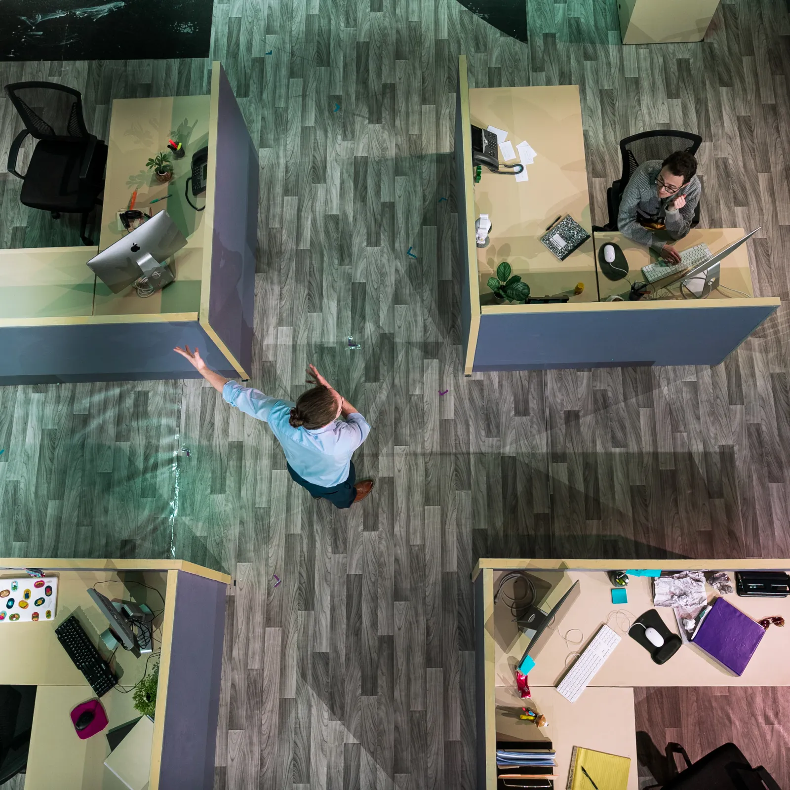 A shot of the set of GLORIA from above, four cubicles sit in a square. There is an individual in the middle of the square gesturing 