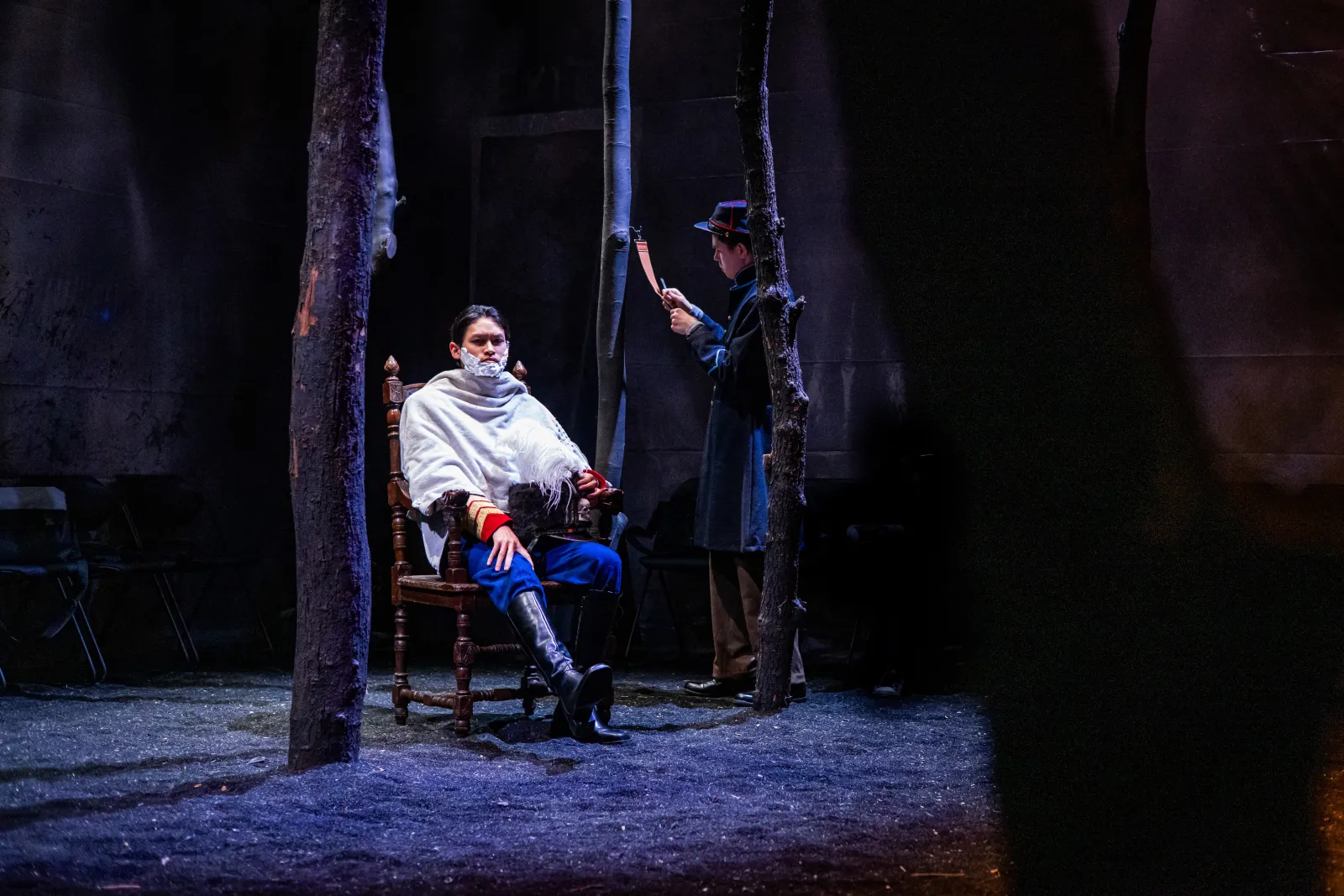 A man is sitting in a chair with shaving cream on his face, while another speaks down to him 