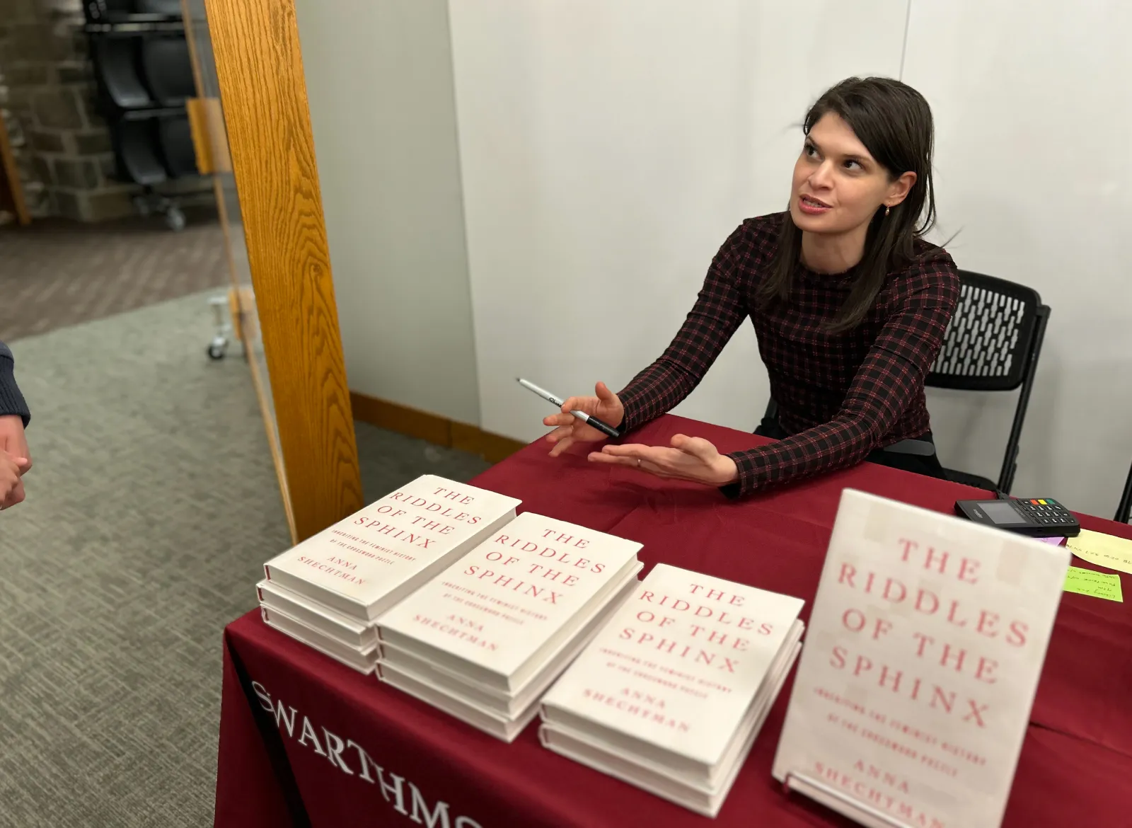 Anna Shechtman sitting at table with red tablecloth with copies of her book to sign.