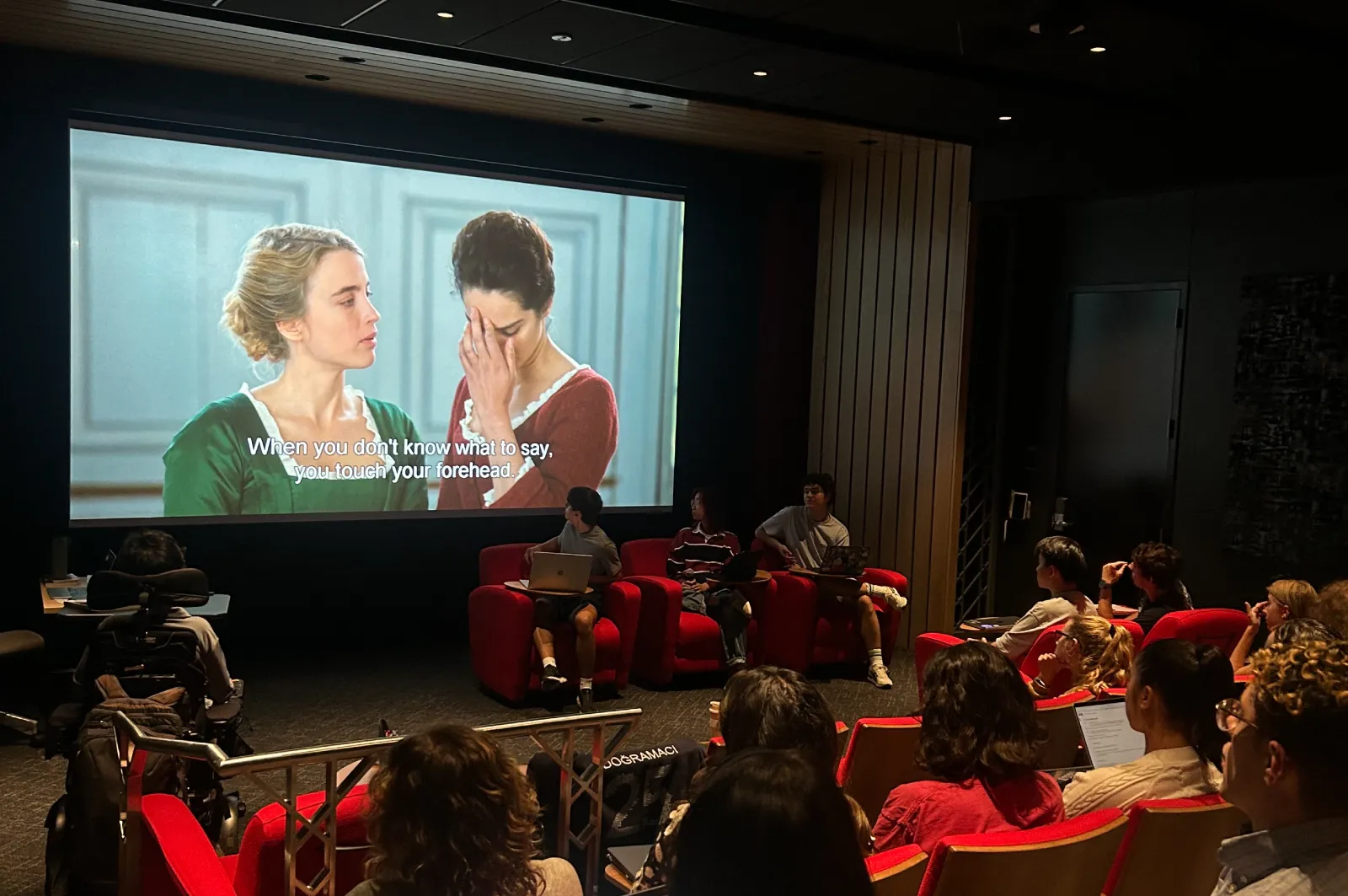 Students sitting in the red chairs in the Chen Screening Room. A scene from Portrait of a Lady on Fire is on the screen