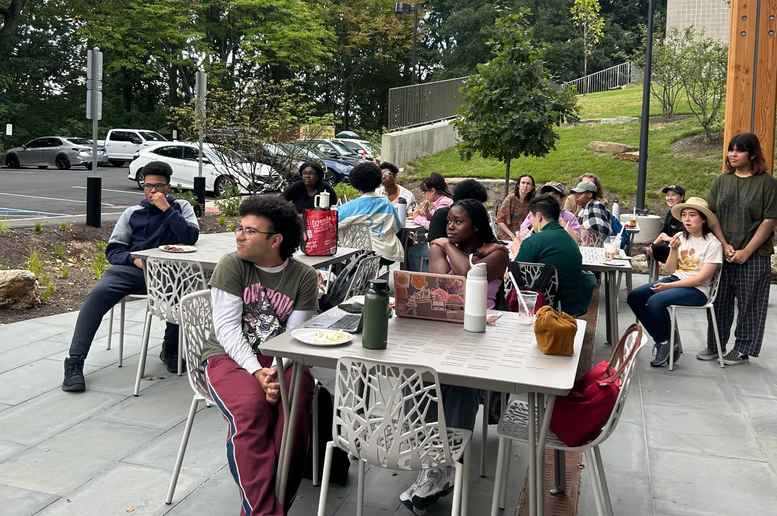 Students sit at tables on the terrace outside Martin Hall. Grass, trees, and parked cars are visible in the background