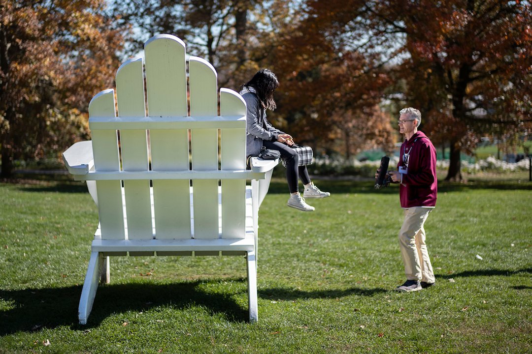 Person sits on large white Adirondack chair