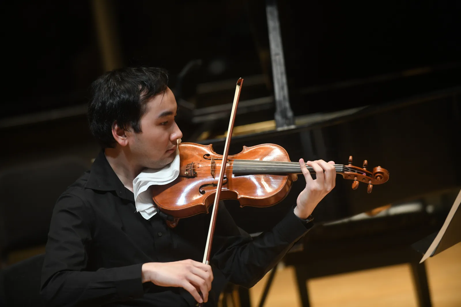 Person in black shirt sits and plays violin or viola
