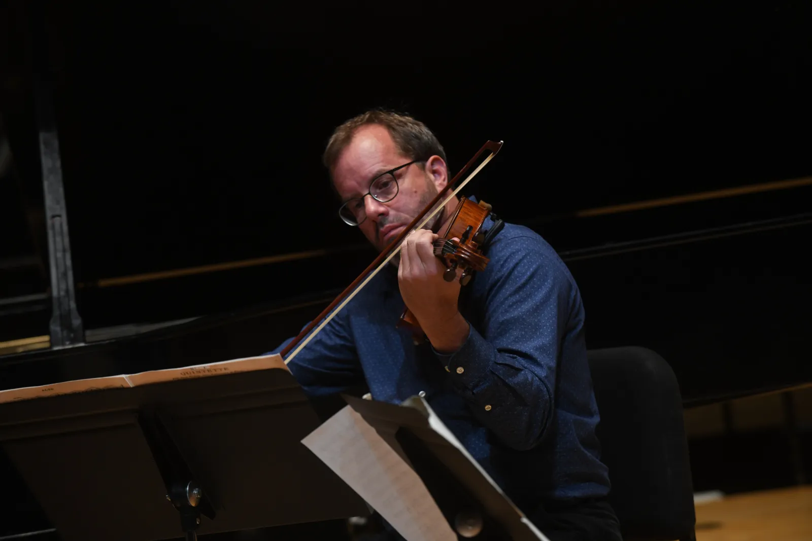 Person sits on stage playing violin or viola