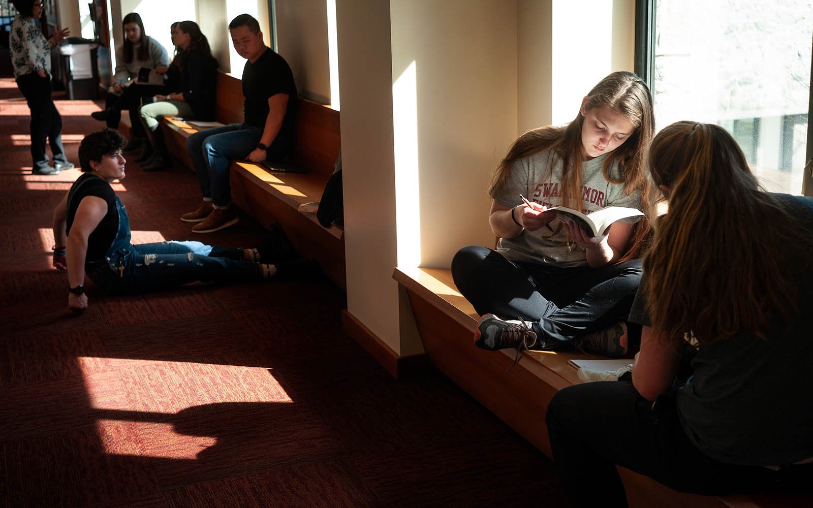 Students reading and lounging in a windowed hallway inside Kohlberg Hall