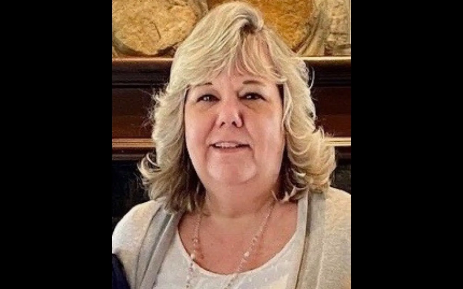 Close shot of a woman with shoulder length blonde hair and bangs wearing a cream-colored top and cardigan.