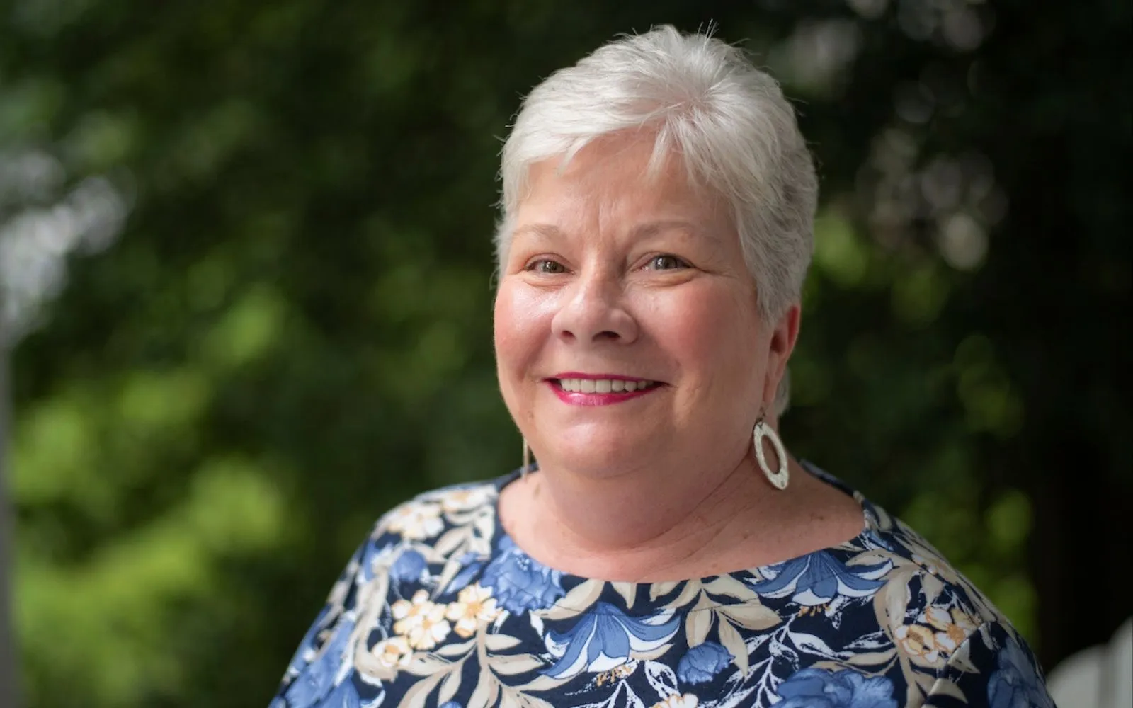 Headshot of a smiling woman with close-cropped white hair, wearing a brightly patterned top.