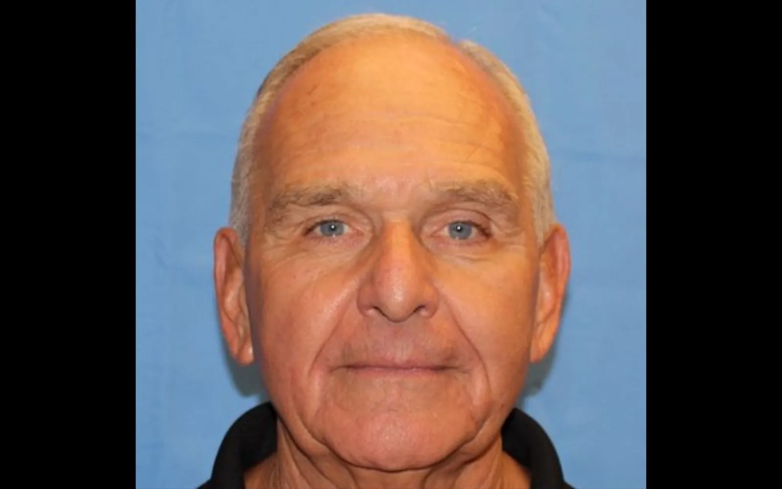 Close shot of a man with close cropped white hair, subtly smiling at the camera.
