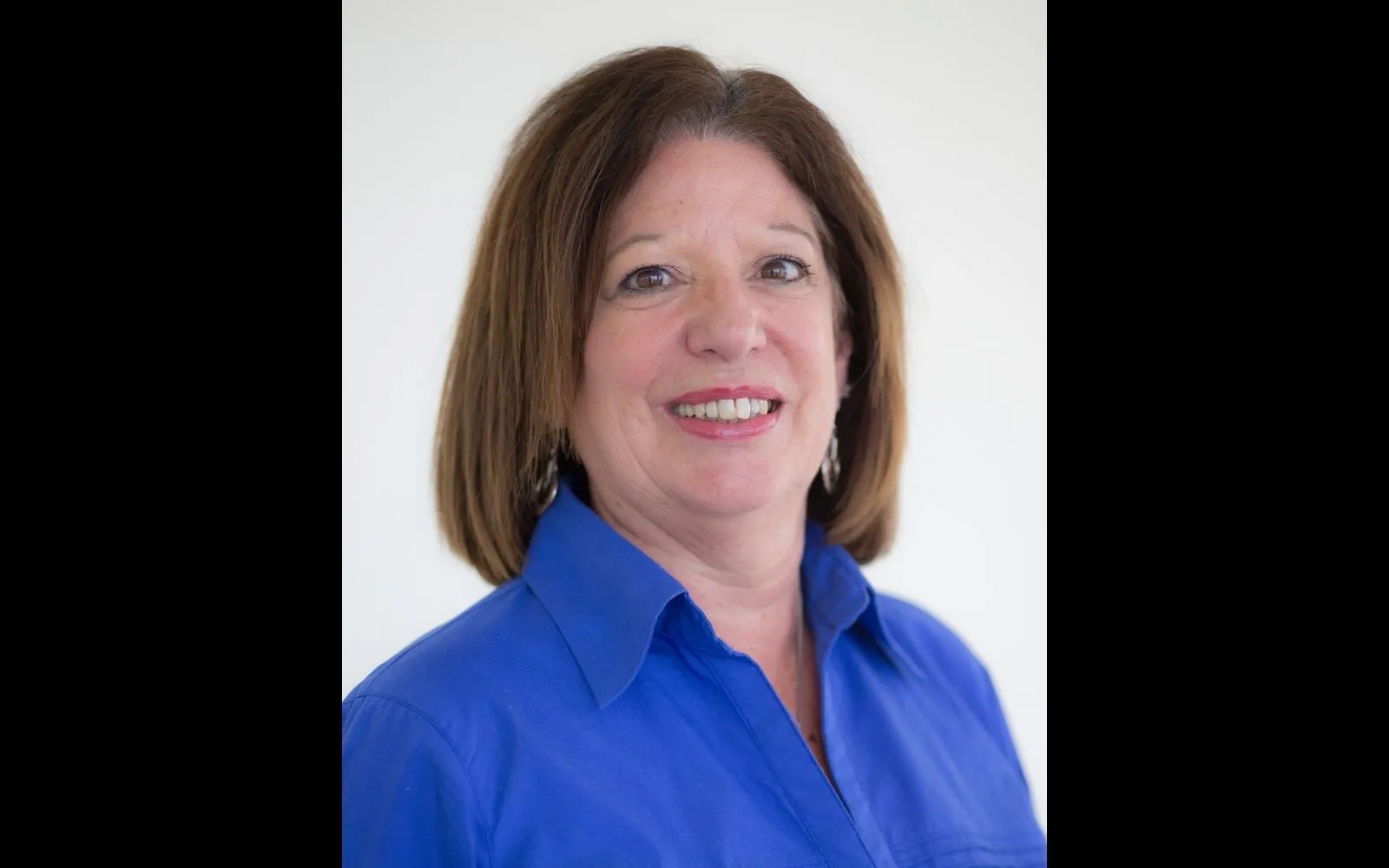 Headshot of a woman with shoulder length brown hair and a bright blue button down shirt.