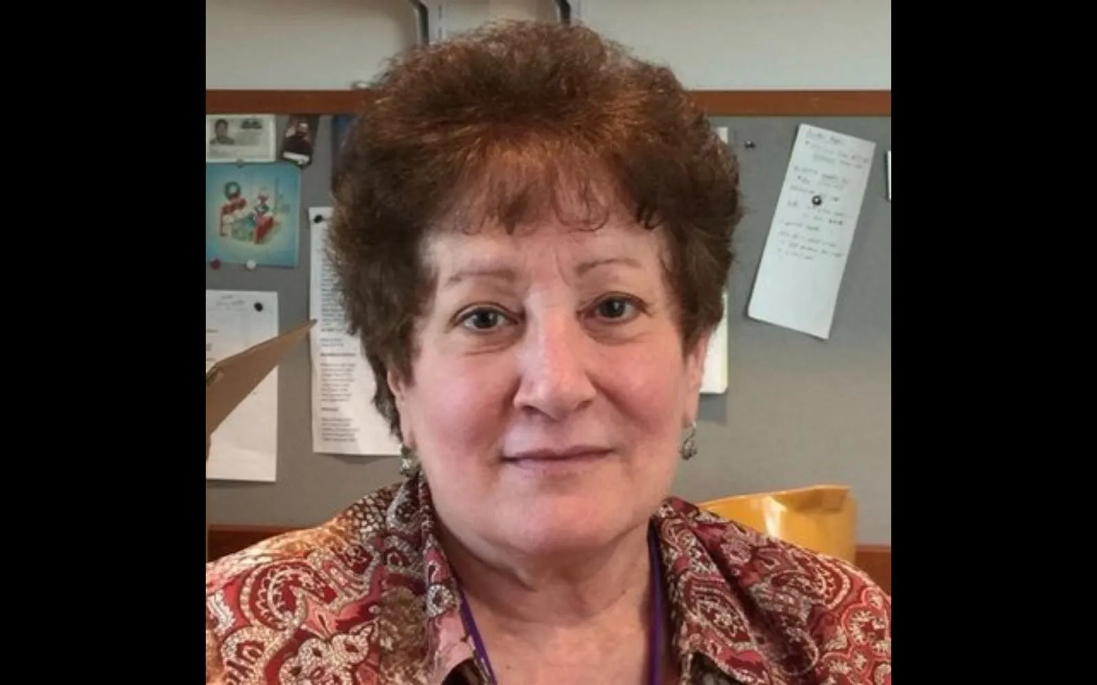 Close shote of a woman with short brown hair and bangs wearing a patterned brown top.