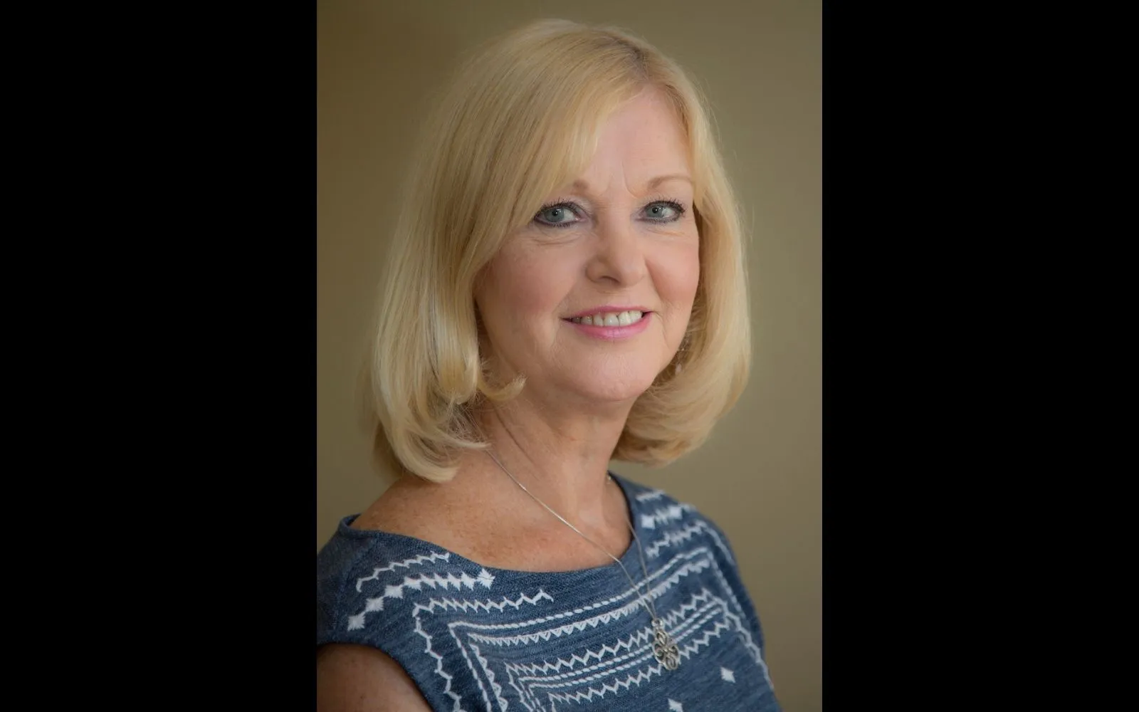 Head shot of a woman with shoulder length blonde hair wearing a striped blue shirt and blue eyeshadow.
