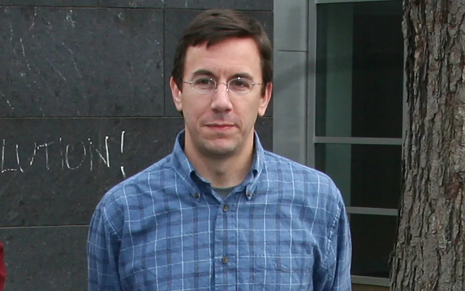 Man with short dark hair and glasses wearing a blue plaid button down.