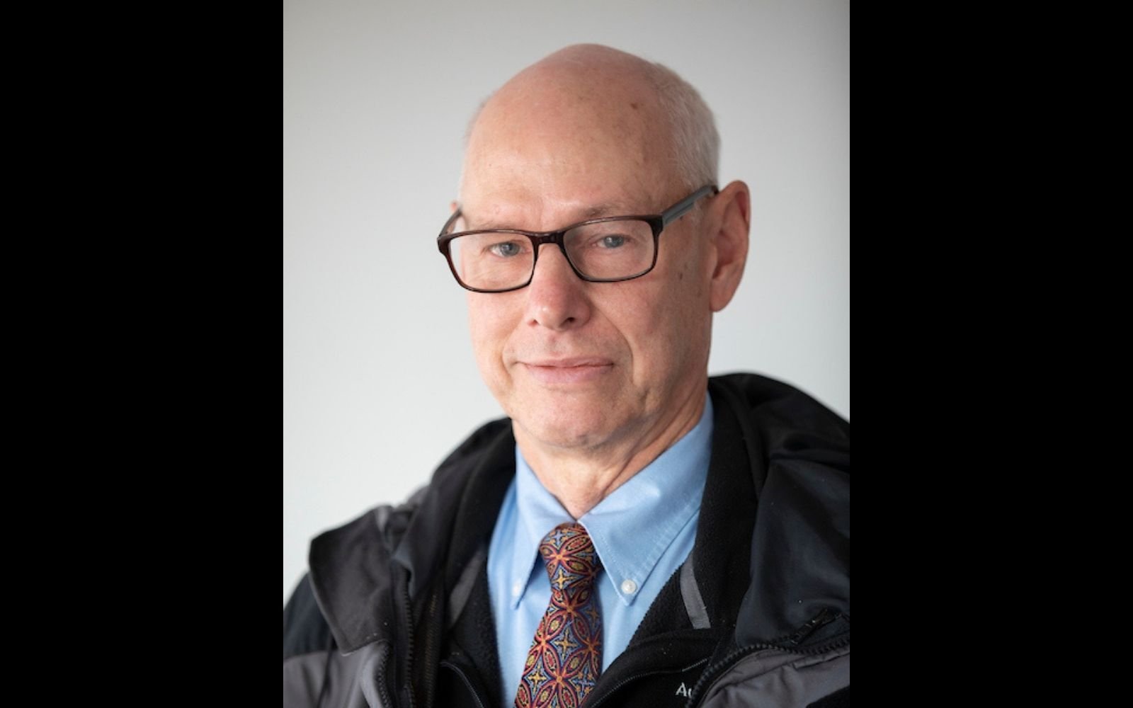 Head shot of bald man with glasses, a red tie, and a blue button down shirt