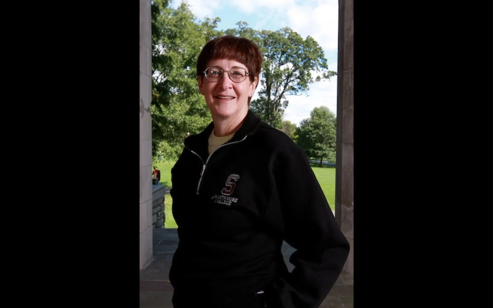 Woman with short brown hair and glasses stands outside in a dark blue sweater and smiles at the camera.