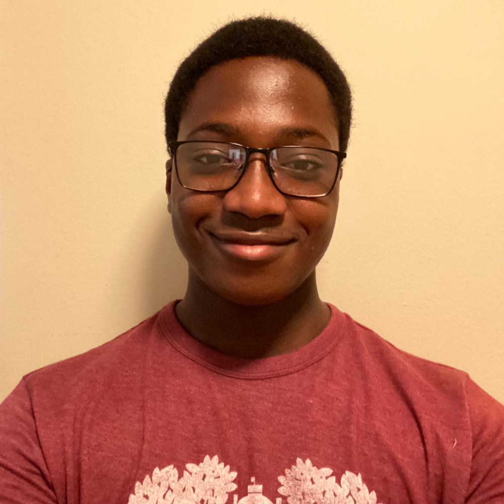 Myles wearing a maroon shirt and classes, smiling in front of a blank wall