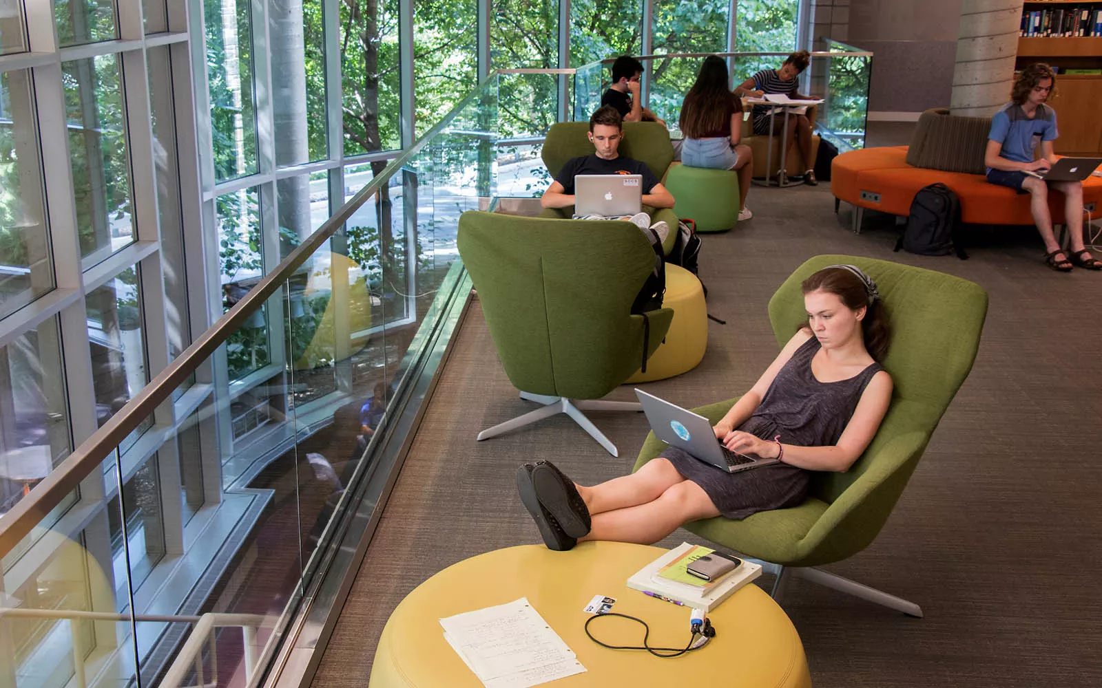 students on computers sitting next to tall windows