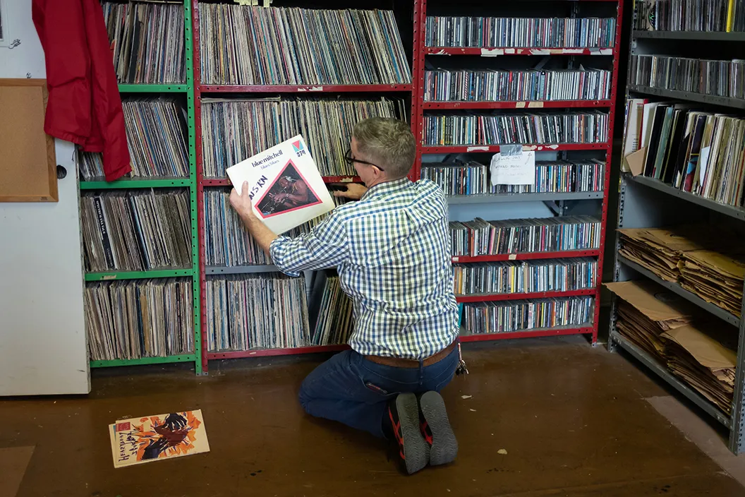 Person holds vinyl record from stack in radio station