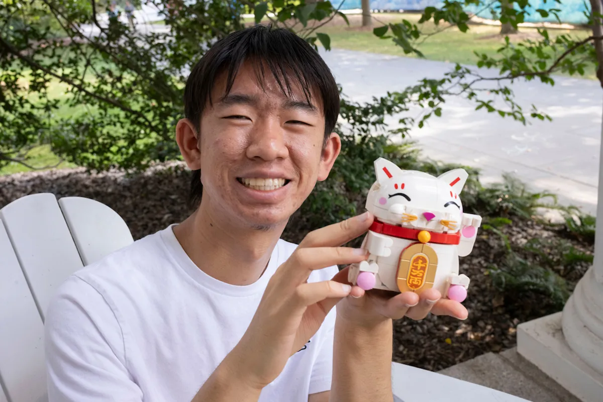 Student helps up lucky white cat made out of legos