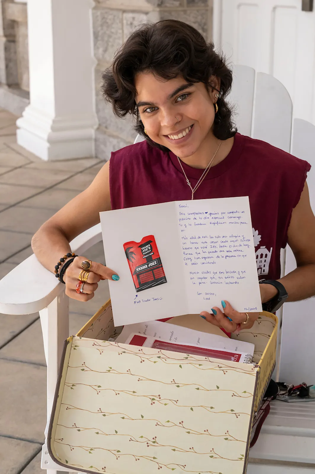 Student holds letter from box while sitting on white Adirondack chair