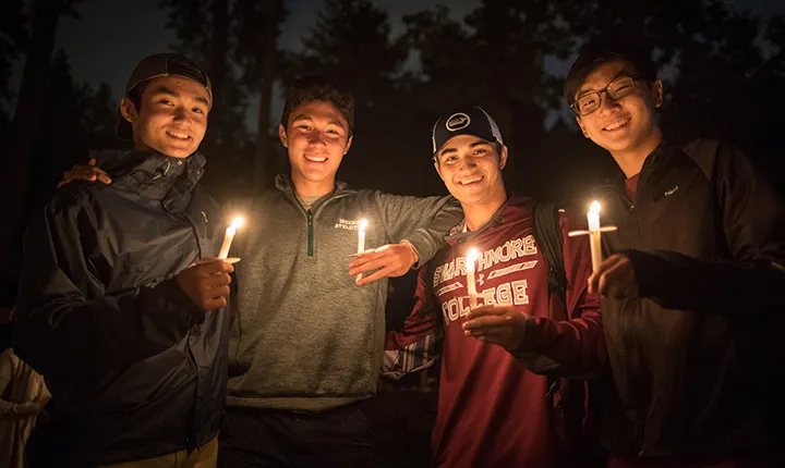 Four students post together holding lit candles