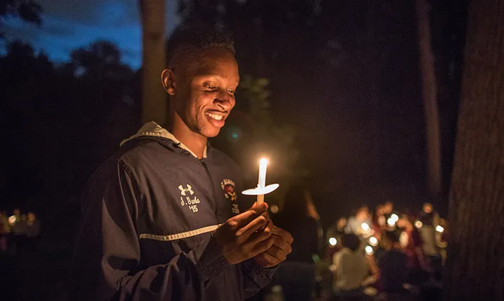 A student looks down and smiles at the candle he is holding