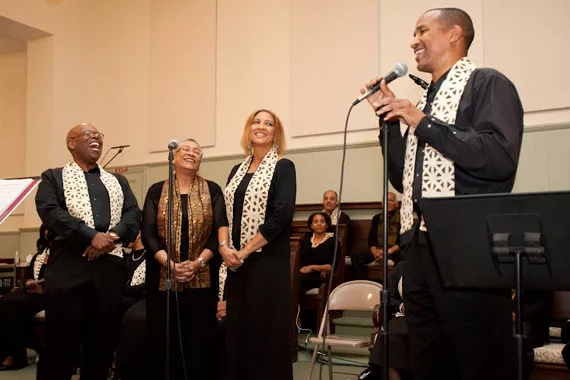 A trio of singers stands in the background with a soloist in the foreground performing