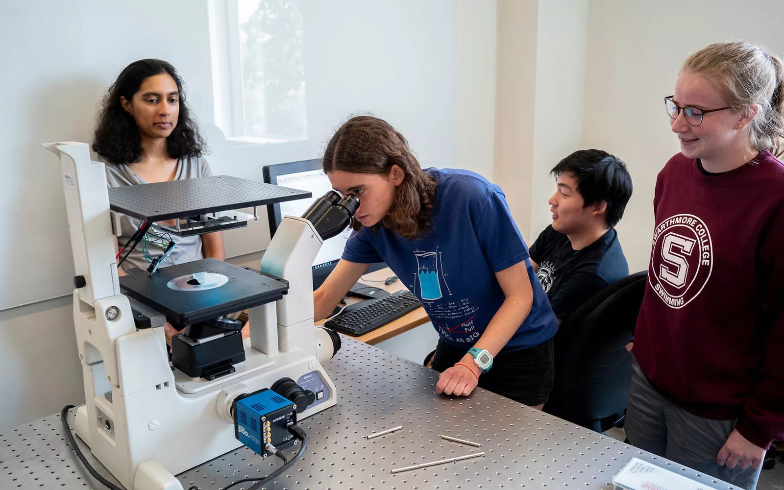 student looking through microscope with 3 students observing