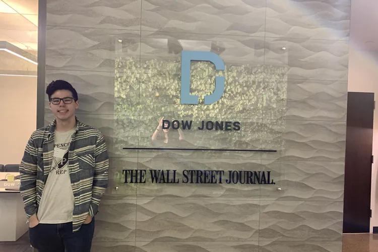Student stands in front of sign that reads "Wall Street Journal"