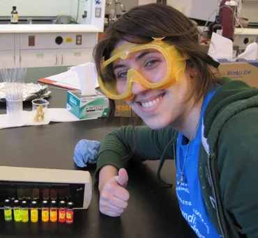 Althea Gaffney, smiling and wearing safety goggles, gives a thumbs up for chemistry