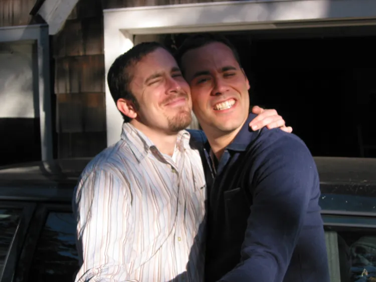 Two white men embracing each other. Quinn Bauriedel '94 on the left wears a pinstripe white shirt, and on the right, Dito wears a blue shirt