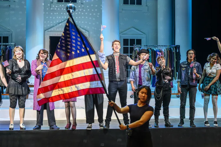 Cast of Threepenny Opera singing the Finale while in the foreground a stagehand waves the american flag