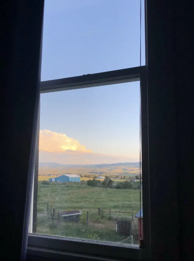 Through a window a farm and mountains in the distance.