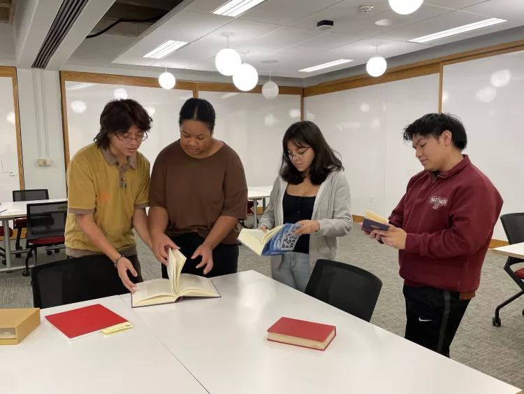 four RIAs standing around a table in LibLab looking at books from the library collection