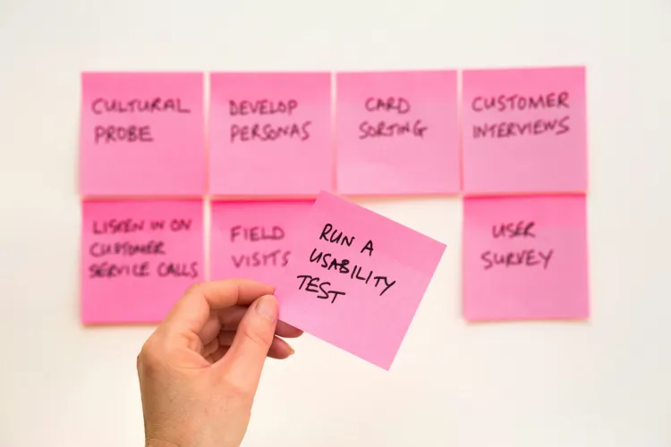 hand applying post it notes listing a variety of user research methods, including run a usability test, to a white board