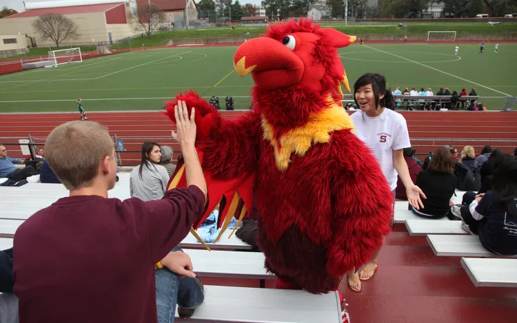 Phineas the Phoenix in bleachers high fiving fan