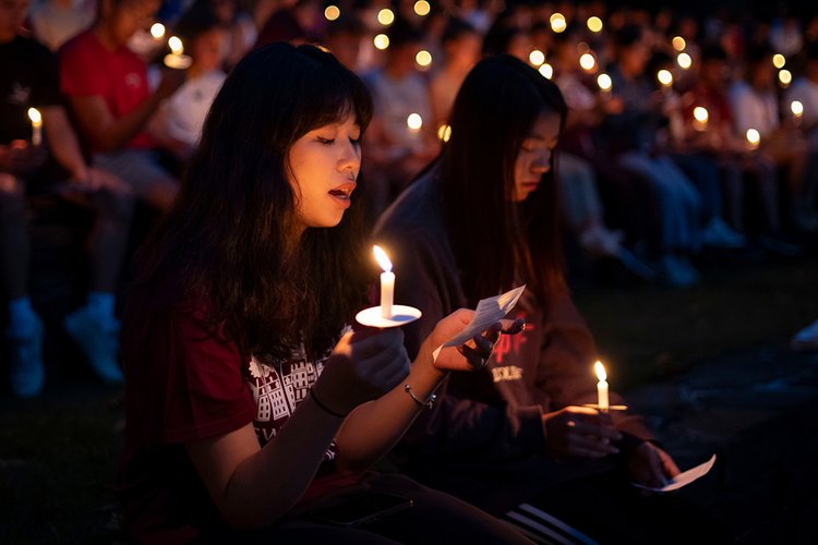 Students holding candles recite alma mater during First Collection