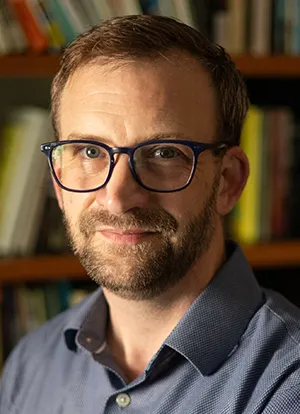 Daniel Laurison wearing glasses, sit in front of bookshelf in office