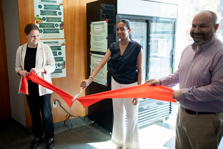 Person with large pair of scissors cuts red ribbon at ceremony