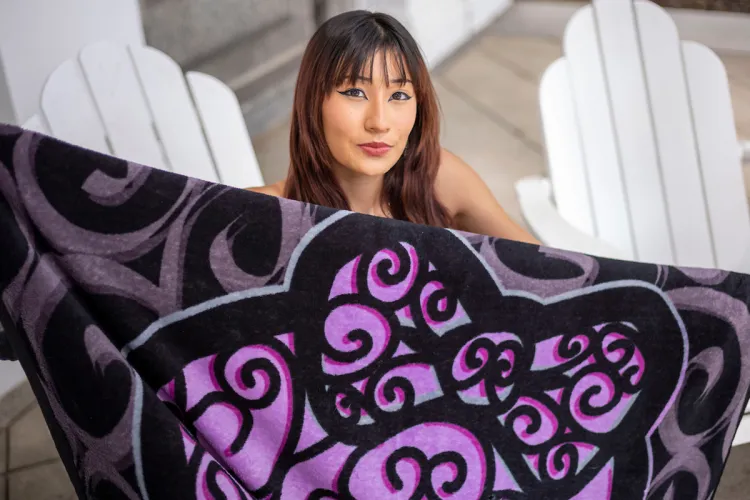 student holds out purple and black blanket while sitting on white Adriondack chair
