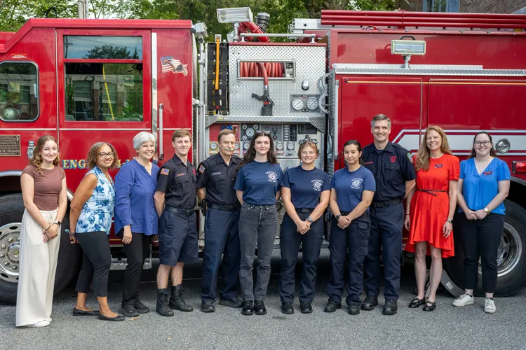 Group of civilians and firefighters pose in front of firetruck