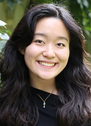 Andrea Cheah stands in front of green leaves