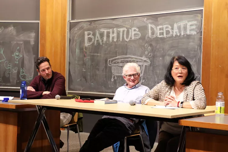 Professors sit in front of blackboard that says "Bathtub Debate"