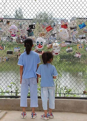 Two individuals look at body of water through a chain link face with masks