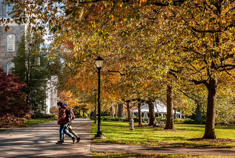 Students walk by stone building in fall