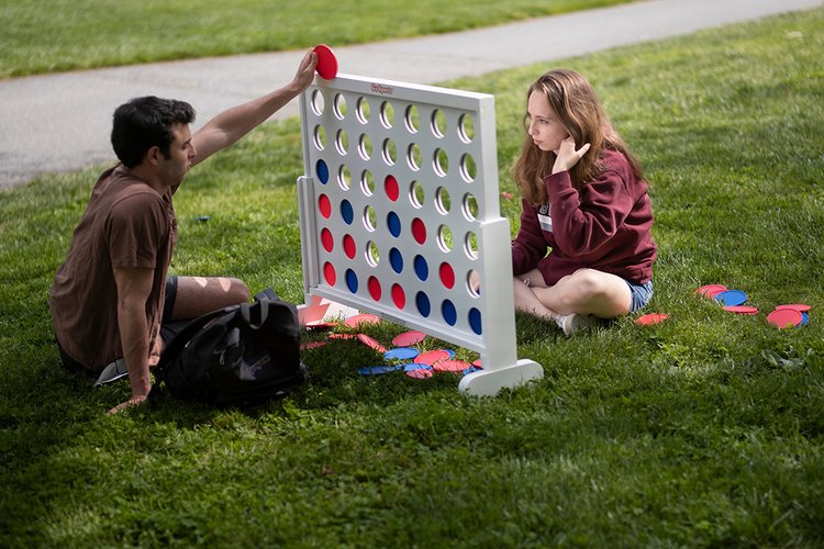 Two people sitting on ground, playing large size connect four game