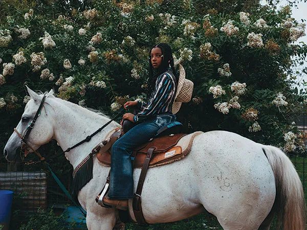 Black woman wearing cowboy attired on white horse 